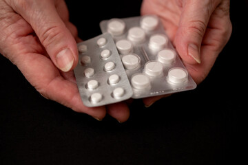 Elderly woman holds pills in her hands.