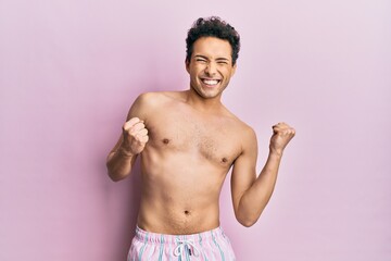 Fototapeta premium Young handsome man wearing swimwear shirtless excited for success with arms raised and eyes closed celebrating victory smiling. winner concept.