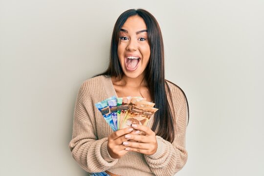 Young Beautiful Hispanic Girl Holding Canadian Dollars Celebrating Crazy And Amazed For Success With Open Eyes Screaming Excited.