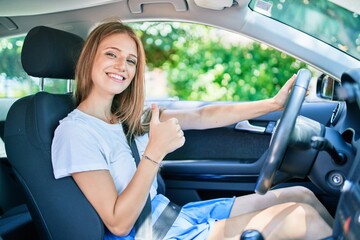 Naklejka premium Young beautiful blonde woman smiling happy driving car with thumb up doing ok sign.