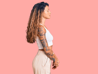 Young hispanic woman with tattoo wearing casual clothes looking to side, relax profile pose with natural face with confident smile.