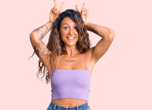 Young hispanic woman with tattoo wearing casual clothes posing funny and crazy with fingers on head as bunny ears, smiling cheerful