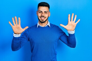 Naklejka premium Young hispanic man with beard wearing casual blue sweater showing and pointing up with fingers number ten while smiling confident and happy.