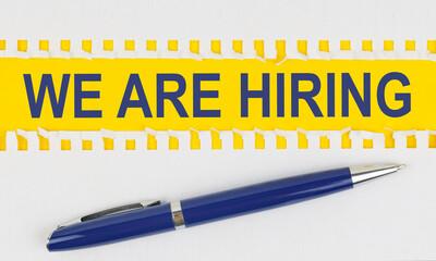 On the table are two sheets from a notebook and a pen on a yellow background written - WE ARE HIRING