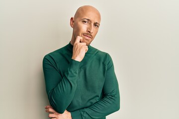 Bald man with beard wearing casual turtleneck sweater thinking concentrated about doubt with finger...