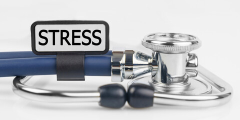 On the white surface lies a stethoscope with a plate with the inscription - STRESS