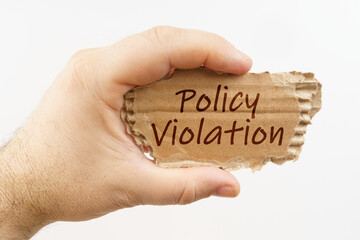 A man holds a cardboard in his hand on which it is written - Policy Violation