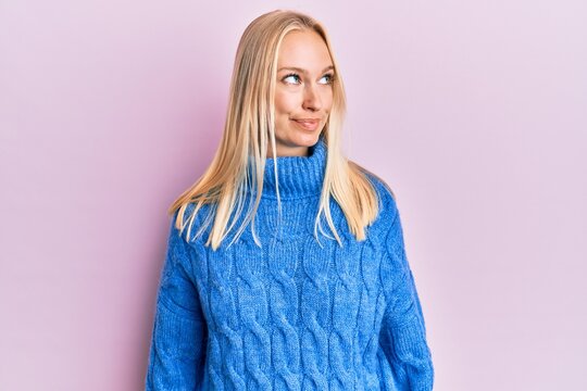 Young blonde girl wearing wool winter sweater smiling looking to the side and staring away thinking.