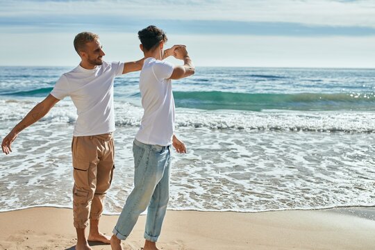 Young gay couple smiling happy dancing at the beach.