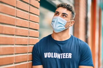 Young hispanic volunteer man wearing medical mask standing at the city.