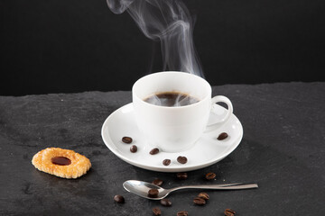 Eine dampfende Tasse Kaffee mit Keks und Kaffeebohnen