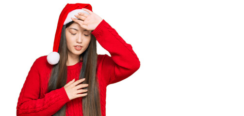 Young chinese woman wearing christmas hat touching forehead for illness and fever, flu and cold, virus sick