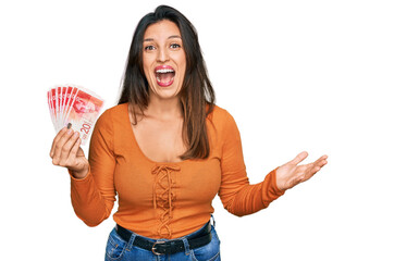 Beautiful hispanic woman holding 20 israel shekels banknotes celebrating victory with happy smile...