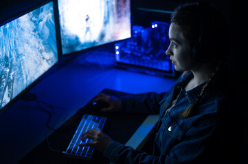 Fototapeta premium A gamer plays for a pc on two large monitors in shooters. Neon light
