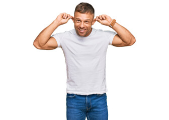 Handsome muscle man wearing casual white tshirt smiling pulling ears with fingers, funny gesture....