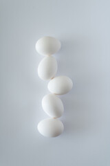 White Easter eggs stacked on top of each other against natural white background in daylight. Minimal flat lay balance concept. Organic food aesthetic composition.