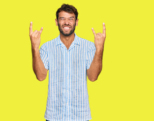 Handsome young man with beard wearing casual fresh shirt shouting with crazy expression doing rock symbol with hands up. music star. heavy concept.