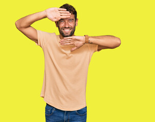 Handsome young man with beard wearing casual tshirt smiling cheerful playing peek a boo with hands showing face. surprised and exited