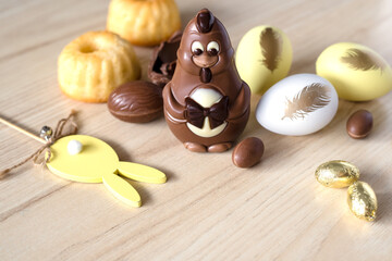 Chocolate Chicken, Easter Cupcakes, Yellow and Chocolate Eggs, Rabbit Decor on wooden background. Easter concept in pastel yellow. Close-up.