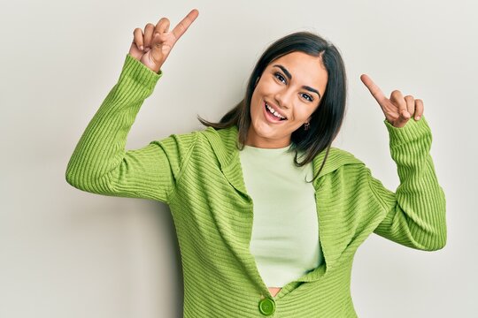 Young brunette woman wearing casual clothes smiling amazed and surprised and pointing up with fingers and raised arms.