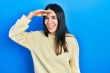 Young brunette woman wearing casual sweatshirt very happy and smiling looking far away with hand over head. searching concept.