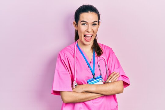 Young brunette woman wearing doctor uniform and stethoscope standing with arms crossed celebrating crazy and amazed for success with open eyes screaming excited.