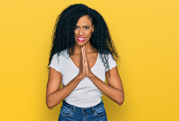 Middle age african american woman wearing casual white t shirt praying with hands together asking for forgiveness smiling confident.