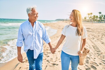Middle age hispanic couple smiling happy walking at the beach.