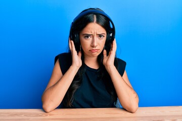 Beautiful brunette young woman listening to music using headphones depressed and worry for distress, crying angry and afraid. sad expression.