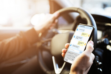 Man Typing Text Message On Phone While Driving Car