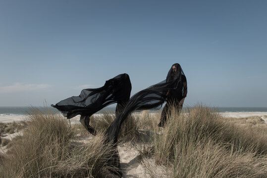 Girl and woman, daughter and mother standing on the dunes near the ocean and beach in black dresses both covered by thin black lace