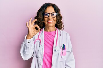 Middle age hispanic woman wearing doctor uniform and glasses smiling positive doing ok sign with...
