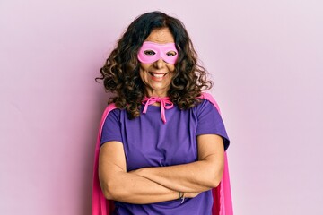 Middle age hispanic woman wearing super hero costume happy face smiling with crossed arms looking...