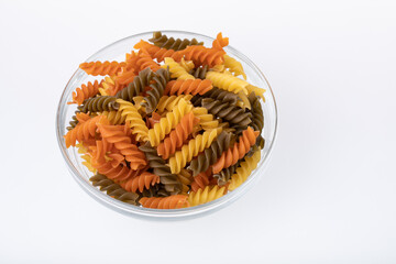 See through glass bowl full with uncooked colorful spiral pasta isolated n white