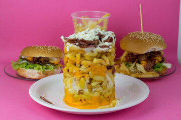 Torre de batata frita com bacon e queijo ralado ao fundo hambúrguer com bacon, queijo e batata...