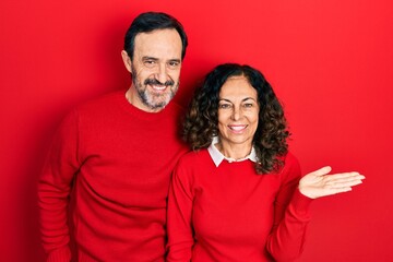 Naklejka premium Middle age couple of hispanic woman and man hugging and standing together smiling cheerful presenting and pointing with palm of hand looking at the camera.
