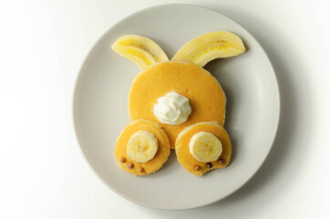 Creative meal for a child, pancake with banana, chocolate and whipped cream in a rabbit shape