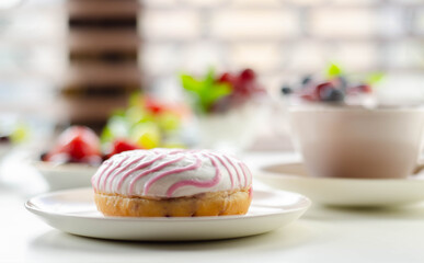 Delicious doughnut topped with white and pink icing served with coffee and fresh fruits