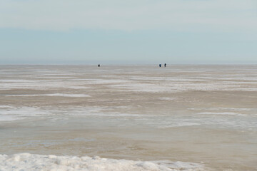 Fototapeta na wymiar On ice of lake in the distance, fishermen are ice fishing in spring