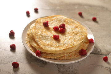homemade pancakes on a white plate with butter decorated with raspberries
