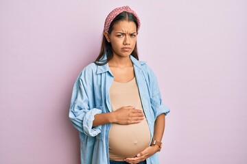 Beautiful hispanic woman expecting a baby, touching pregnant belly skeptic and nervous, frowning upset because of problem. negative person.