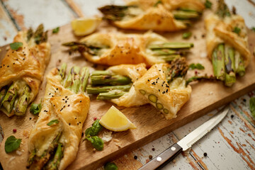 Baked green asparagus wrapped in puff pastry. Served on wooden board. With selective focus