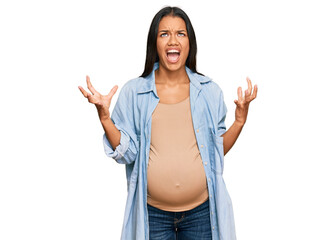 Beautiful hispanic woman expecting a baby showing pregnant belly crazy and mad shouting and yelling with aggressive expression and arms raised. frustration concept.