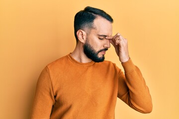 Young man with beard wearing casual winter sweater tired rubbing nose and eyes feeling fatigue and headache. stress and frustration concept.