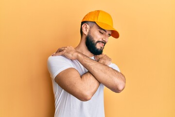 Young man with beard wearing yellow cap hugging oneself happy and positive, smiling confident. self love and self care