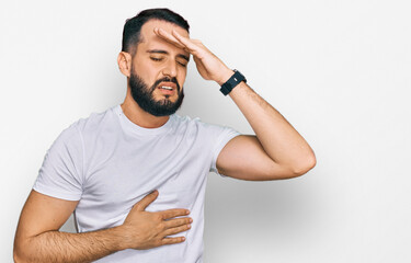 Young man with beard wearing casual white t shirt touching forehead for illness and fever, flu and cold, virus sick