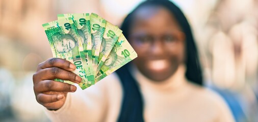 Young african american woman smiling happy holding south africa rands banknotes at the city.