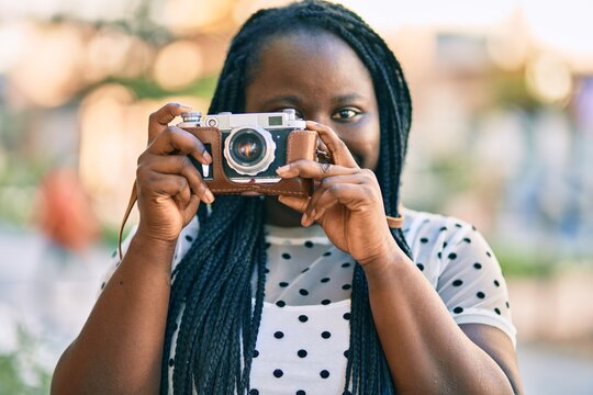 Young african american tourist woman smiling happy using vintage camera at the city.