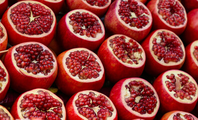 Fresh sweet red pomegranates cut in half at a farmers market. Delicious fruits on a stall are beautifully laid out on the counter of the store: cut and cleaned. Natural organic food background.