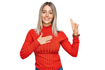Beautiful blonde woman wearing casual clothes smiling swearing with hand on chest and fingers up,...